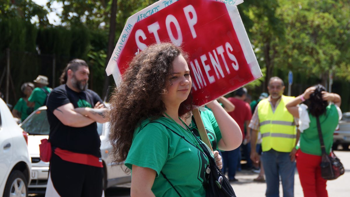 Una noia amb samarreta verda de la PAH subjecta un senyal de "Stop Desnonaments"